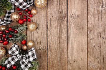 Christmas side border with white and black checked buffalo plaid ribbon, decorations and tree branches. Overhead view on a rustic wood background.
