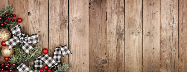 Christmas corner border banner with white and black checked buffalo plaid ribbon, baubles and tree branches. Above view on a rustic wood background.
