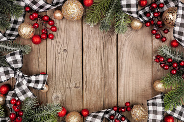 Christmas frame with white and black checked buffalo plaid ribbon, baubles and tree branches. Top view on a rustic wood background.