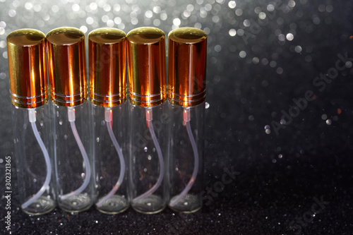 Fotografia Five glass tall perfume atomizers on a dark shiny background
