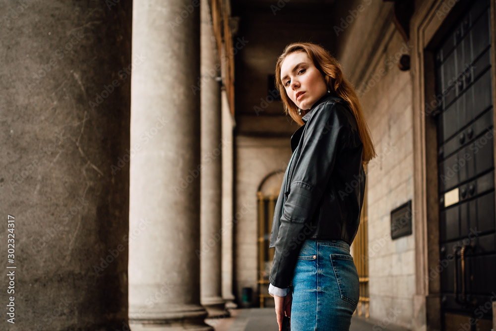 young lovely girl in leather jacket and jeans resting outdoors, portrait of woman with beautiful hair in the city