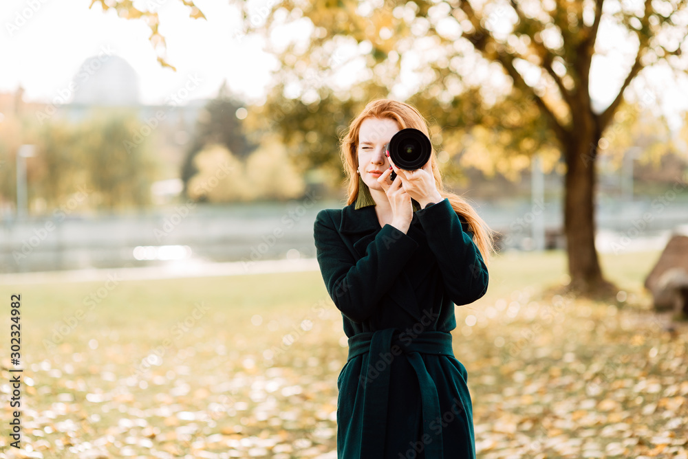 portrait of cute cheerful young girl with amazing red hair posing outdoors holding camera, redhead woman is relaxing on the park