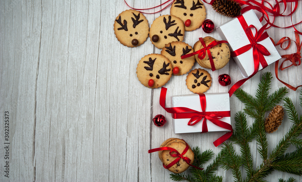 Christmas composition.Gift boxes, homemade gingerbread in the form of Santa's reindeer, fir branches and cones, red ribbons and bells on a light wooden background. Christmas, winter, New year.