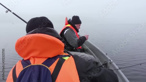 Father and son fishing on small boat dense fog on lake in Finland