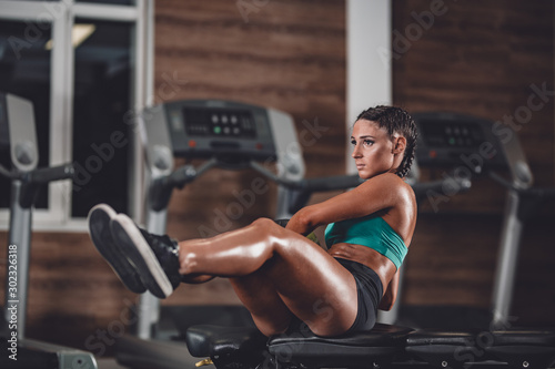 Slim dark-haired girl dressed in sports clothes doing exercises for the press on the mat for fitness with fitness ball in the gym