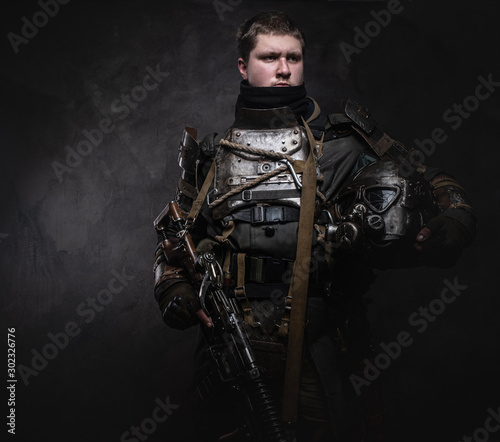 Foto Portrait of young serious man in doomsday warrior's costume at dark photo studio