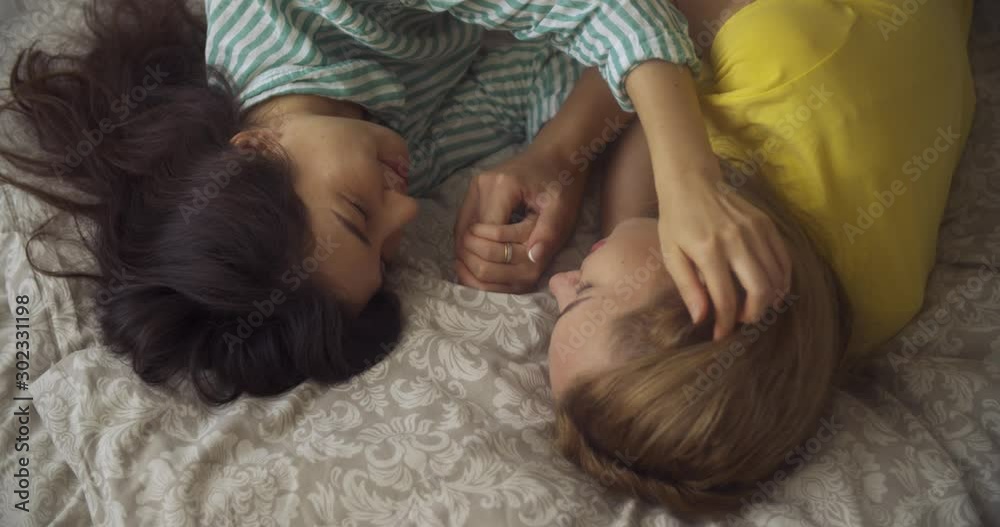 two multinational yong women lesbians lie in the bedroom on the bed and caress each other. LGBT two multinational yong women lesbians lie in the bedroom on the bed and caress each other. LGBT