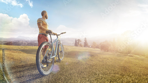 Cycling. Man with bike on a forest road in the mountains on a summer day. Mountain valley during sunrise. Sport