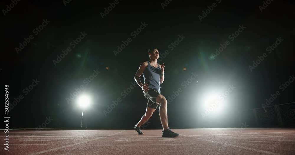 A professional athlete warming up and stretching before start of evening training on stadium, spotted by lights on black background - sports concept 4k footage