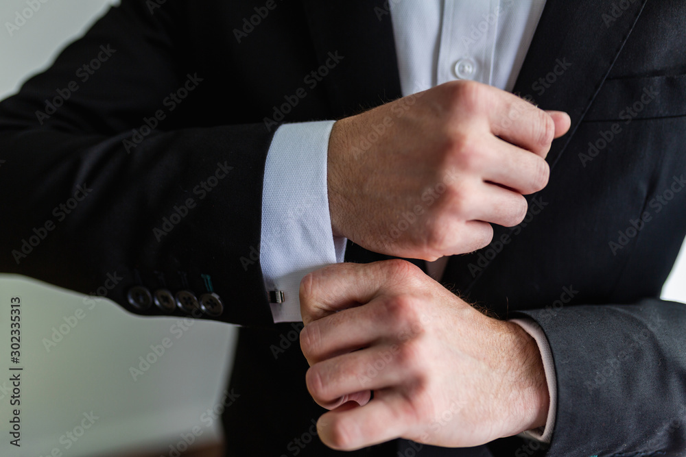 Businessman in an expensive black suit fixes cufflinks on his white shirt. A man in a classic suit adjusts the cuffs of his shirt. Successful business concept