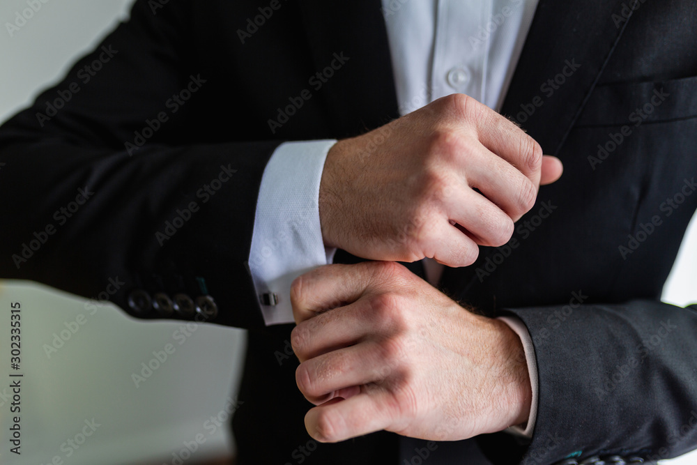 Businessman in an expensive black suit fixes cufflinks on his white shirt. A man in a classic suit adjusts the cuffs of his shirt. Successful business concept