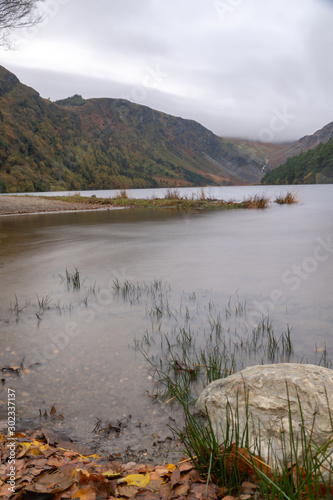 Long exposuire view, silky water during autumn in the Wicklow Mountains. Rock on front, Glendalough Upper lake covered with mist and fog in upper part, calm water, view from low angle photo