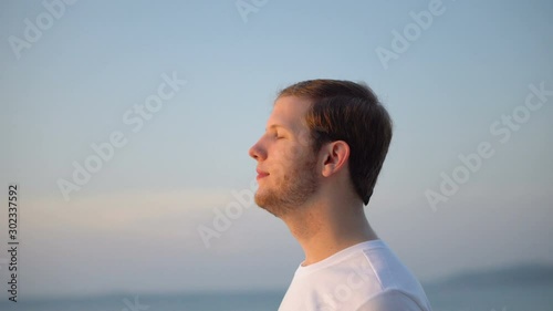 Portrait of Happy Man Breathing in Deeply and Looking at Beautiful Sunset Over Ocean photo