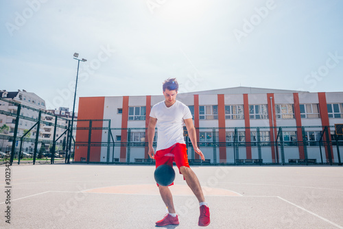 Strong male basketball player preparing for a basketball game on a sunny day wearing a white tee and red shorts.