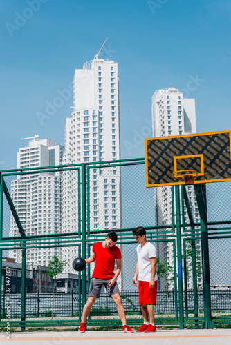 Basketball players playing ball(pushing, dribbling) on an urban basketball ground while the white skyscrapers nearly touch the blue sky.