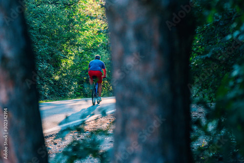 Older cyclist in his mid-40s riding a bike on a road through the woods and looking extremely tired.