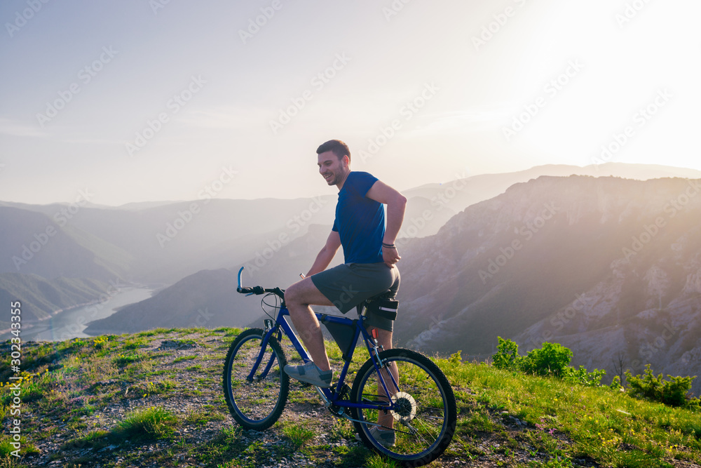 Fototapeta premium Adventurous Cyclist riding his mountain bike at the edge of a cliff, on rocky terrain while wearing no safety equipment.Amazing top view.