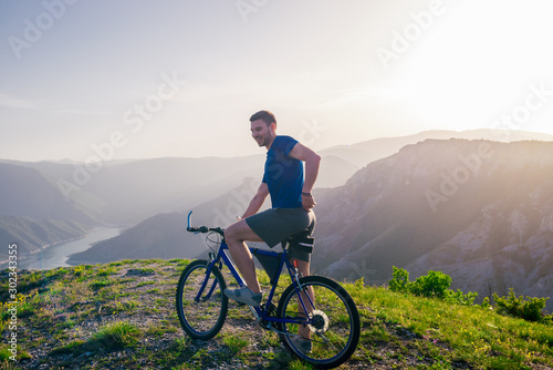 Adventurous Cyclist riding his mountain bike at the edge of a cliff, on rocky terrain while wearing no safety equipment.Amazing top view. © qunica.com