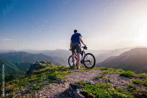 Fototapeta Naklejka Na Ścianę i Meble -  Adventurous Cyclist riding his mountain bike at the edge of a cliff, on rocky terrain while wearing no safety equipment.Amazing top view.
