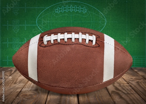 American football ball on wooden table on green wall