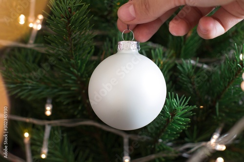 young woman hanging white christmas ornament on christmas tree photo