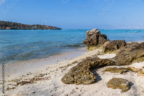 Weathered rocks on white sand beach, Nusa lembongan, Bali, Indonesia. Clear blue ocean with boats beyond. Neighboring island of Nusa Penida in the distance.  photo