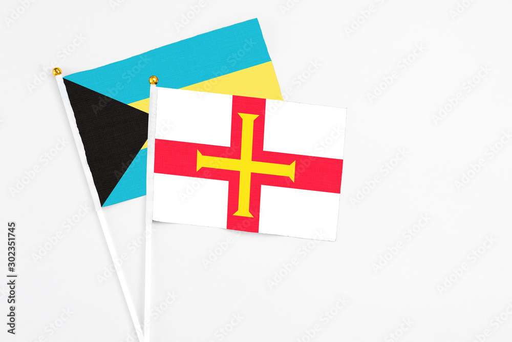 Guernsey and Bahamas stick flags on white background. High quality fabric, miniature national flag. Peaceful global concept.White floor for copy space.