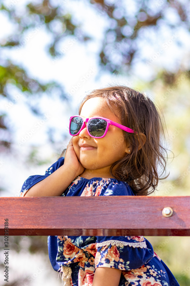Cute little girl with pink sunglasses and hands on her face.