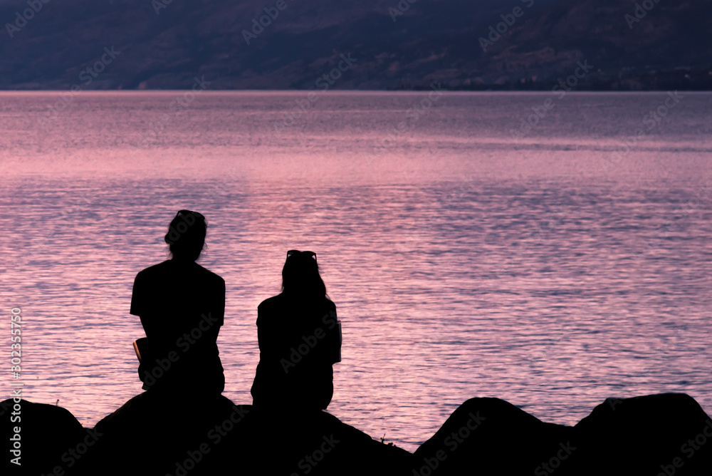Close-up silhouettes of man and woman sitting together on beach watching sunset