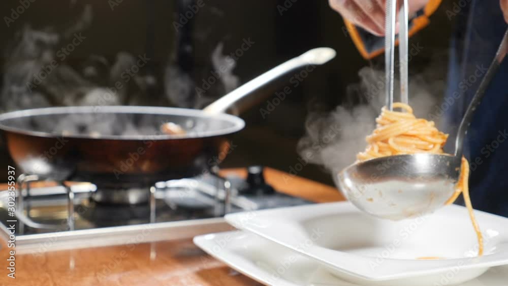 Chef serving pasta on plate. Close up. Putting pasta in plate with kitchen tongues and laddle. Italian cuisine. White steam rising in slow mo. Shot in hd Chef serving pasta on plate. Close up. Putting pasta in plate with kitchen tongues and laddle. Italian cuisine. White steam rising in slow mo. Shot in hd