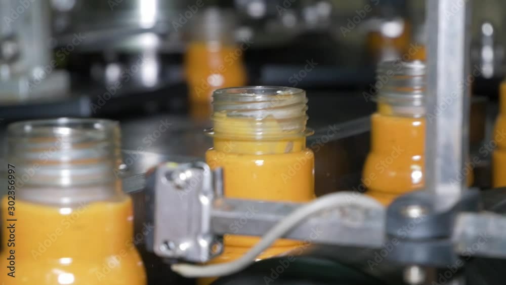 Bottles filled with sauce moving to a cap filler machine. Bottles filled with sauce moving to a cap filler machine.
