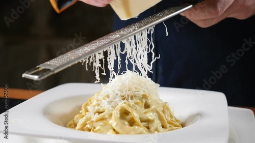 Foodvideo footage shot in slow motion. Cheese is being grated on the plate of freshly-cooked Italian pasta. Chef grating hard cheese. Cooking seafood pasta. Shot in hd photo
