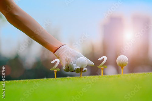 Hand of woman golfer laying golf ball onto wooden tee on tee off in the golf course with welcoming year 2020 celebration and greeting season through the year.