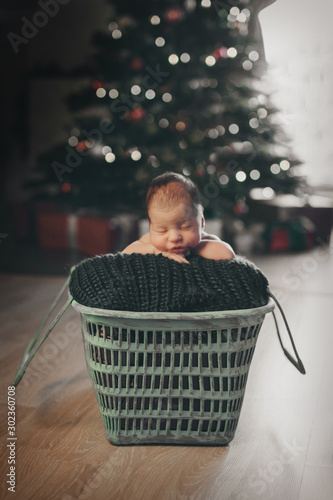 newborn baby in a hat sleeping in a crib on the background of Christmas trees . Imitation of a baby in the womb. Portrait of a newborn. healthy lifestyle concept, IVF Christmas, new year holidays