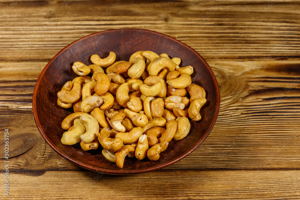 Ceramic plate with roasted cashew nuts on a wooden table Ceramic plate with roasted cashew nuts on a wooden table