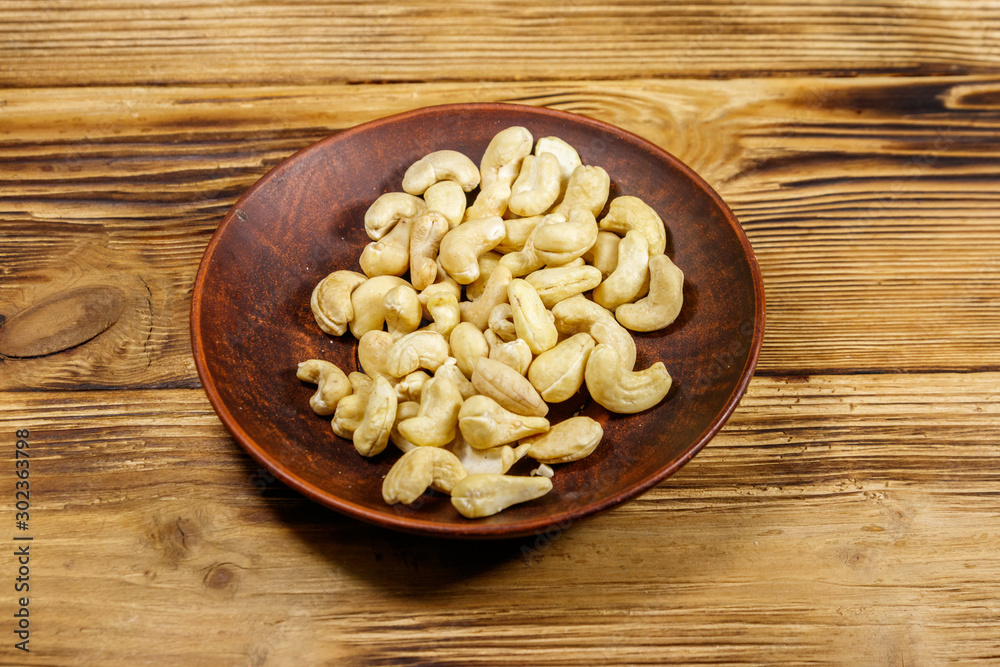Ceramic plate with raw cashew nuts on a wooden table Ceramic plate with raw cashew nuts on a wooden table