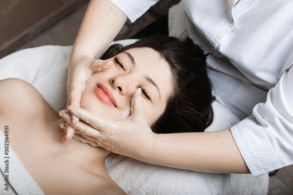 Upper view portrait of a lovely young woman having facial massage by a cosmetologist in a spa center. Upper view portrait of a lovely young woman having facial massage by a cosmetologist in a spa center.