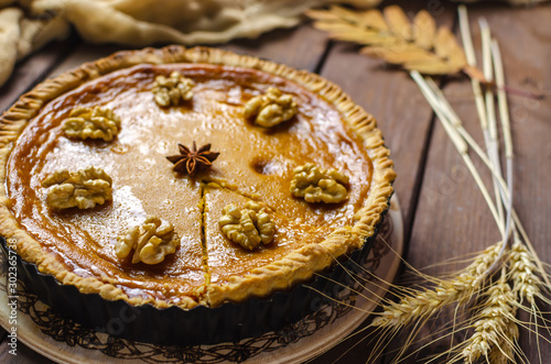 Pumpkin homemade vegan pie and spices cinnamon, anis, yelllow dry autumn leaves decor on dark table background.