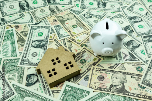 Small wooden house and piggy bank on a pile of ten dollar banknotes, Money background