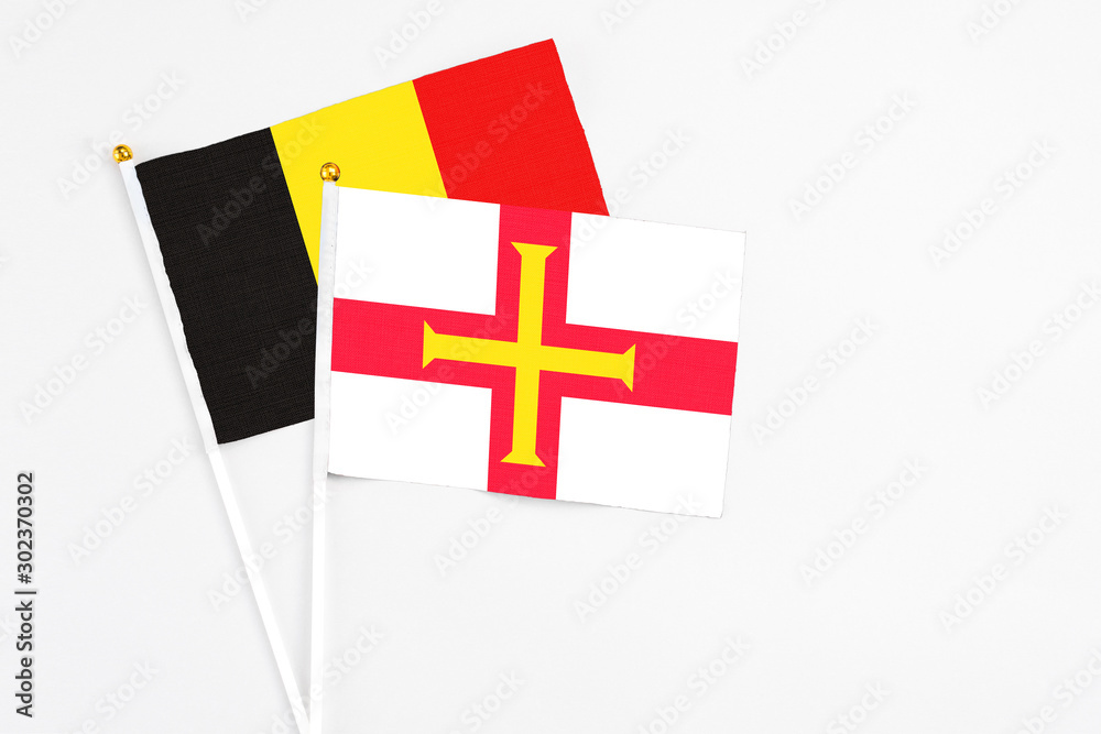 Guernsey and Belgium stick flags on white background. High quality fabric, miniature national flag. Peaceful global concept.White floor for copy space.