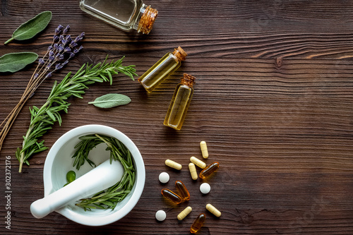 Medicine made from wildflowers and herbs with essential oils -pattern with mortar and pestle on dark wooden background top view copy space