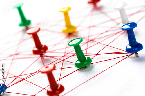 Network with colorful pins and string, linked together with string on a white background suggesting a network of connections.