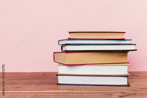 A simple composition of many hardback books, raw books on a wooden table and a pale pink background