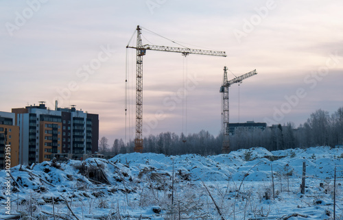 Winter season tower cranes on the construction of a buildings, in the background of the forest and all in the snow