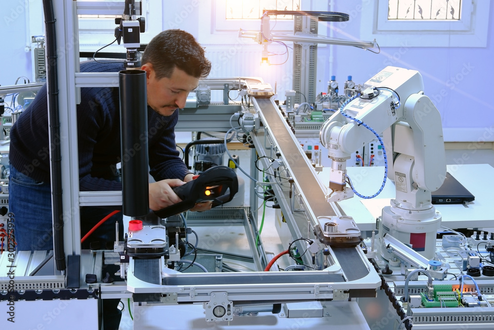 Industry 4.0 concept: An engineer is programming robotic arm with control panel (teach pendant) which is working on smart factory production line. Selective Focus. Industry 4.0 concept: An engineer is programming robotic arm with control panel (teach pendant) which is working on smart factory production line. Selective Focus.