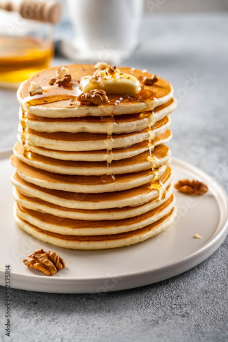 Tasty breakfast. Homemade pancakes with crushed walnut, honey or maple syrup on grey background.