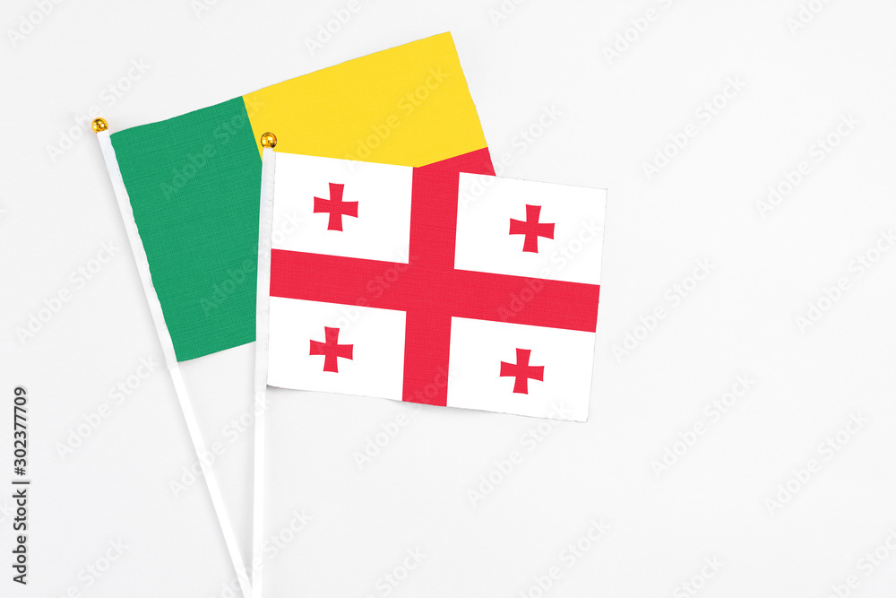 Georgia and Benin stick flags on white background. High quality fabric, miniature national flag. Peaceful global concept.White floor for copy space.