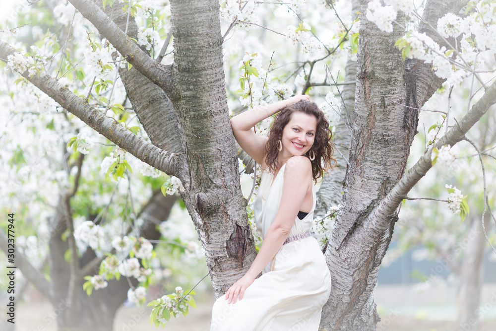A portrait of beautiful young Caucasian woman with curly dark hair in blossoming orchard A portrait of beautiful young Caucasian woman with curly dark hair in blossoming orchard