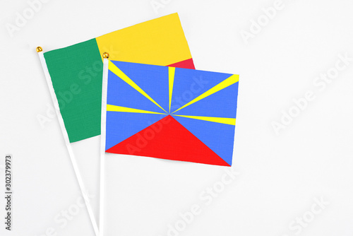 Reunion and Benin stick flags on white background. High quality fabric, miniature national flag. Peaceful global concept.White floor for copy space.