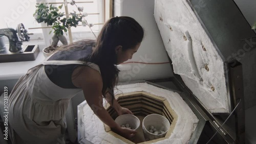 Female potter puts a clay pot in a kiln photo